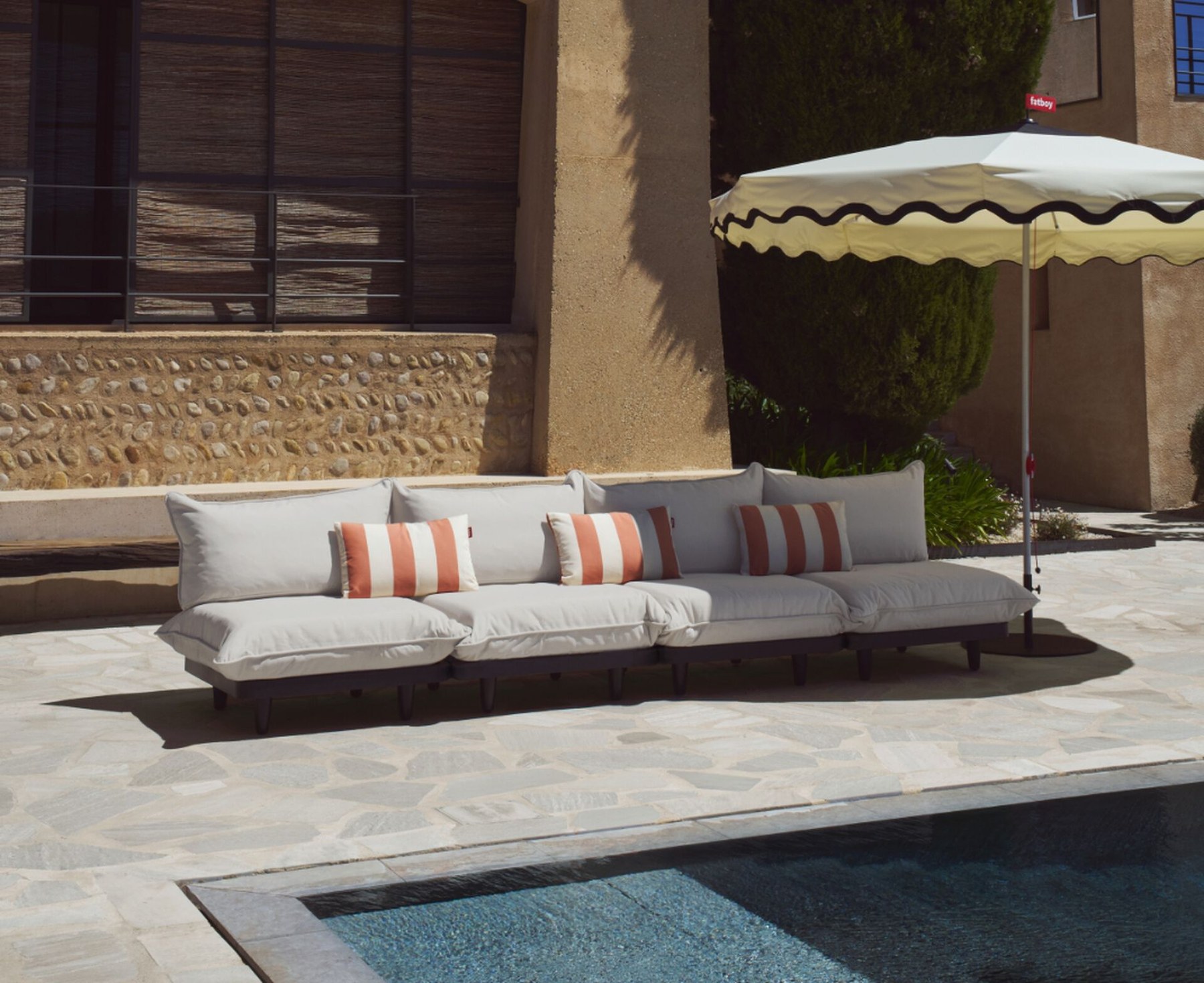 Fatboy outdoor sofa beside a pool with striped cushions and umbrella